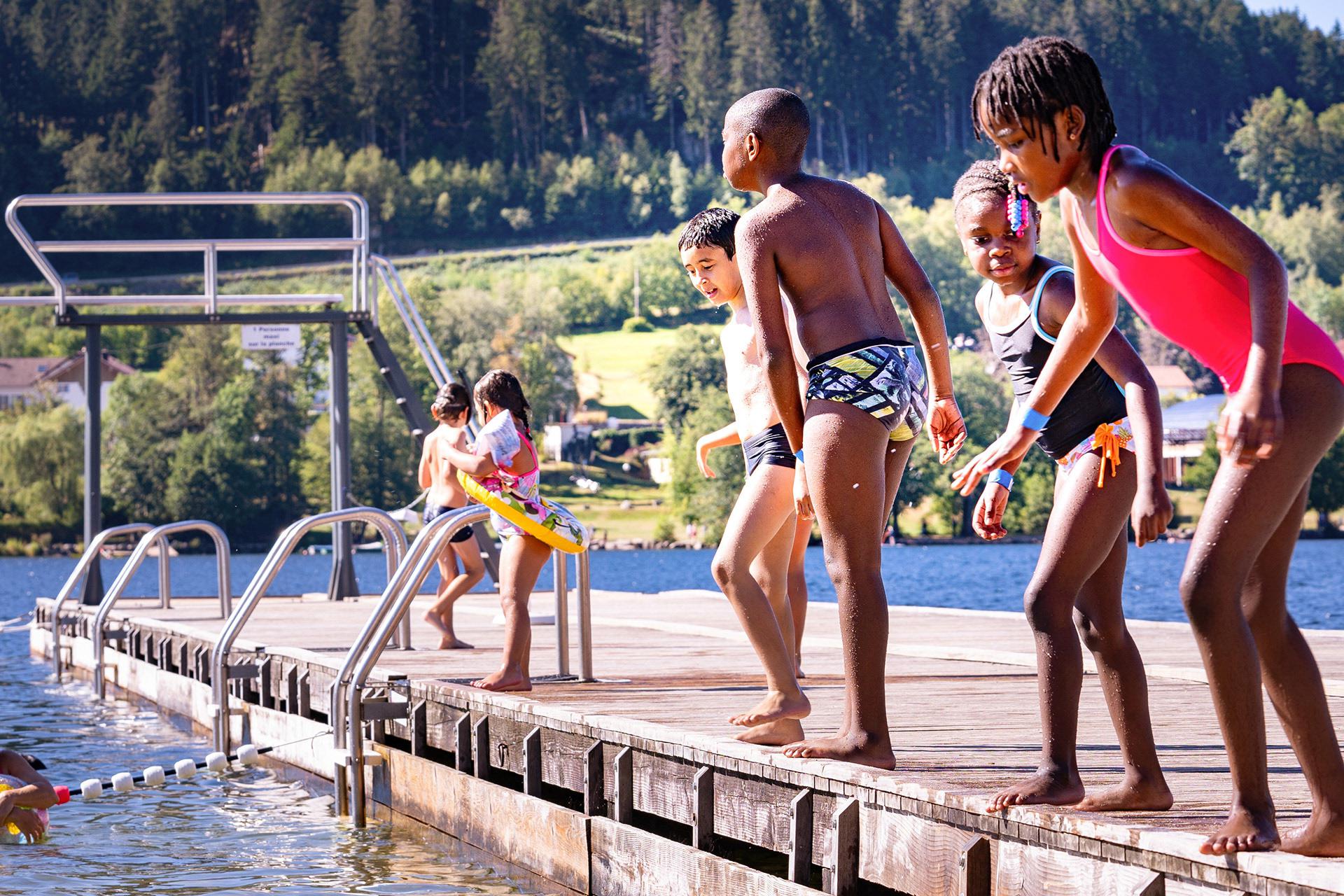 Les enfants s'amusent à sauter dans l'eau du lac de Gérardmer de la petite jetée boisée
