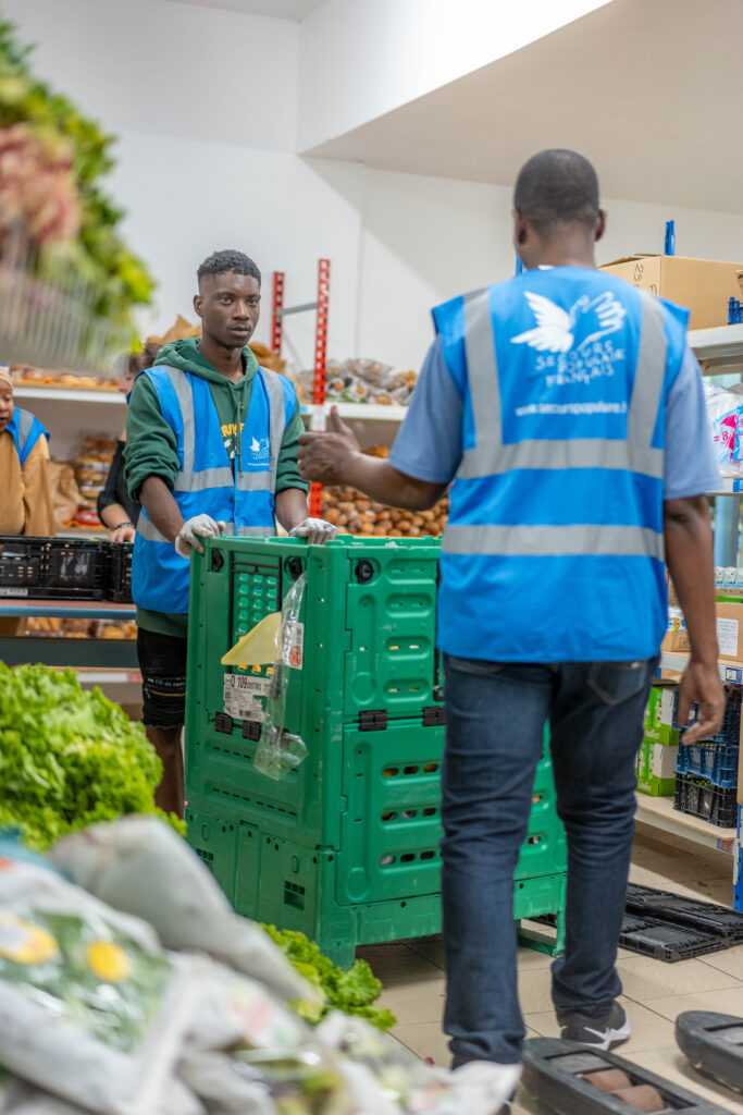 Deux bénévoles dont l'un est de dos discutent ensemble autour d'un chariot de distribution.