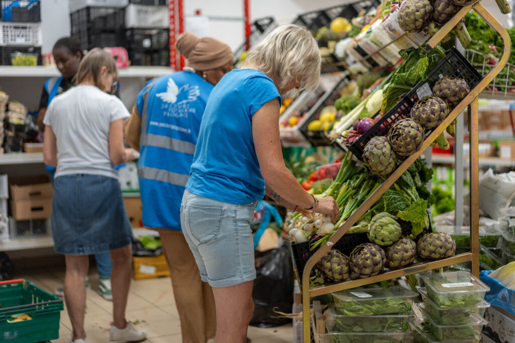 Une femme aidée prend des oignons blancs sur une étale de légumes.