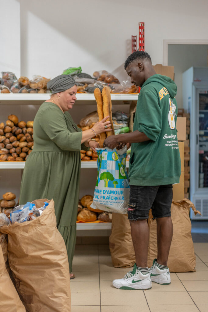 Deux bénéficiaires rangent des baguettes de pain dans un sac.