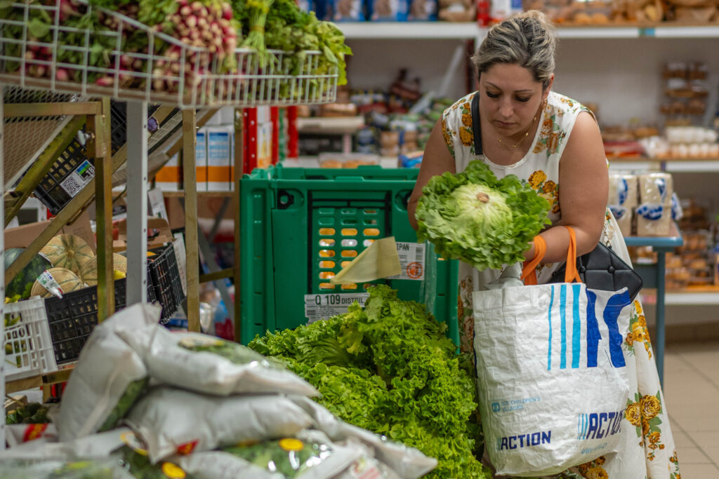 Une femme bénéficiaire de l'aide alimentaire choisit une salade à mettre dans son sac de courses.