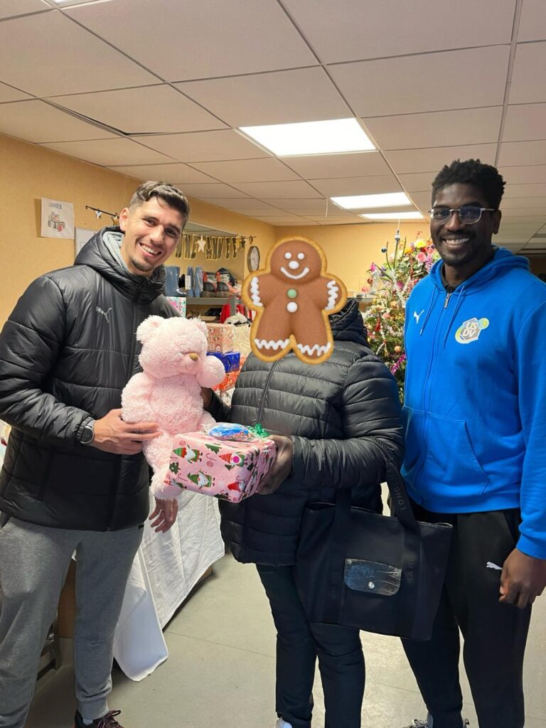 deux handballeurs qui remettent des boites de Noël et des  peluches à une maman pour ses enfants.